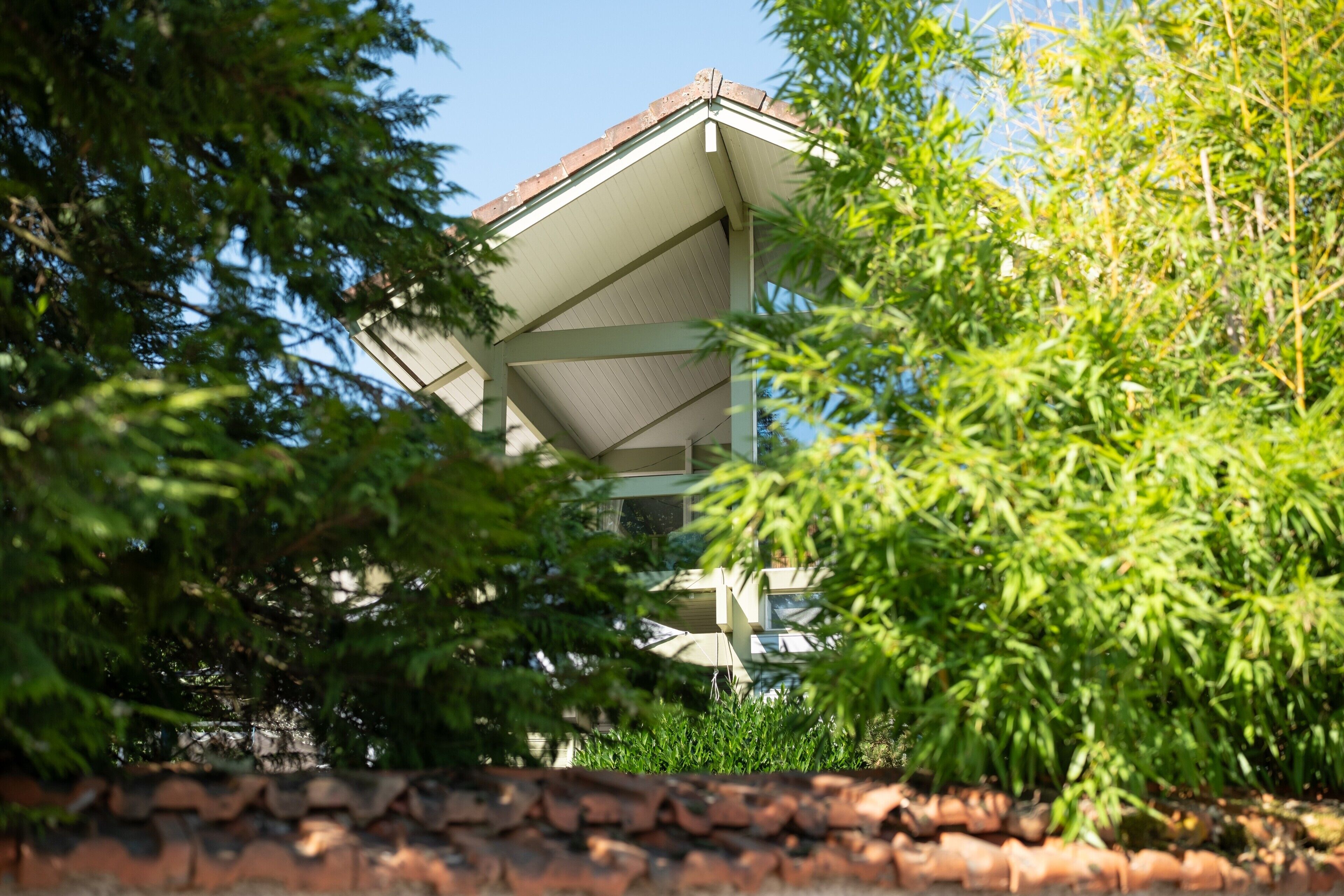 Un bâtiment doté d’un toit en pente, entouré de verdure.
