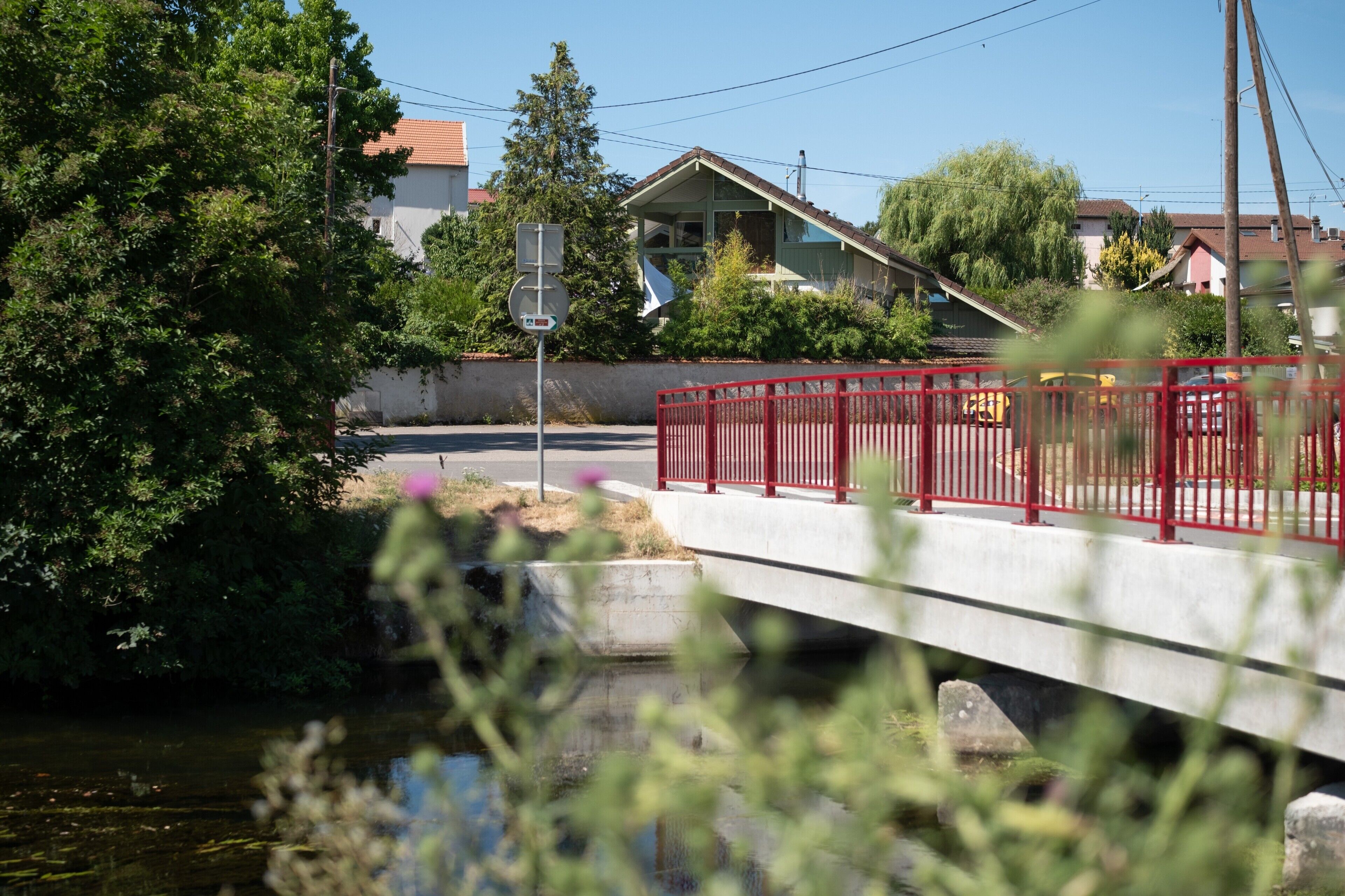 Un pont avec une rambarde rouge, un ciel dégagé et des maisons en arrière-plan.