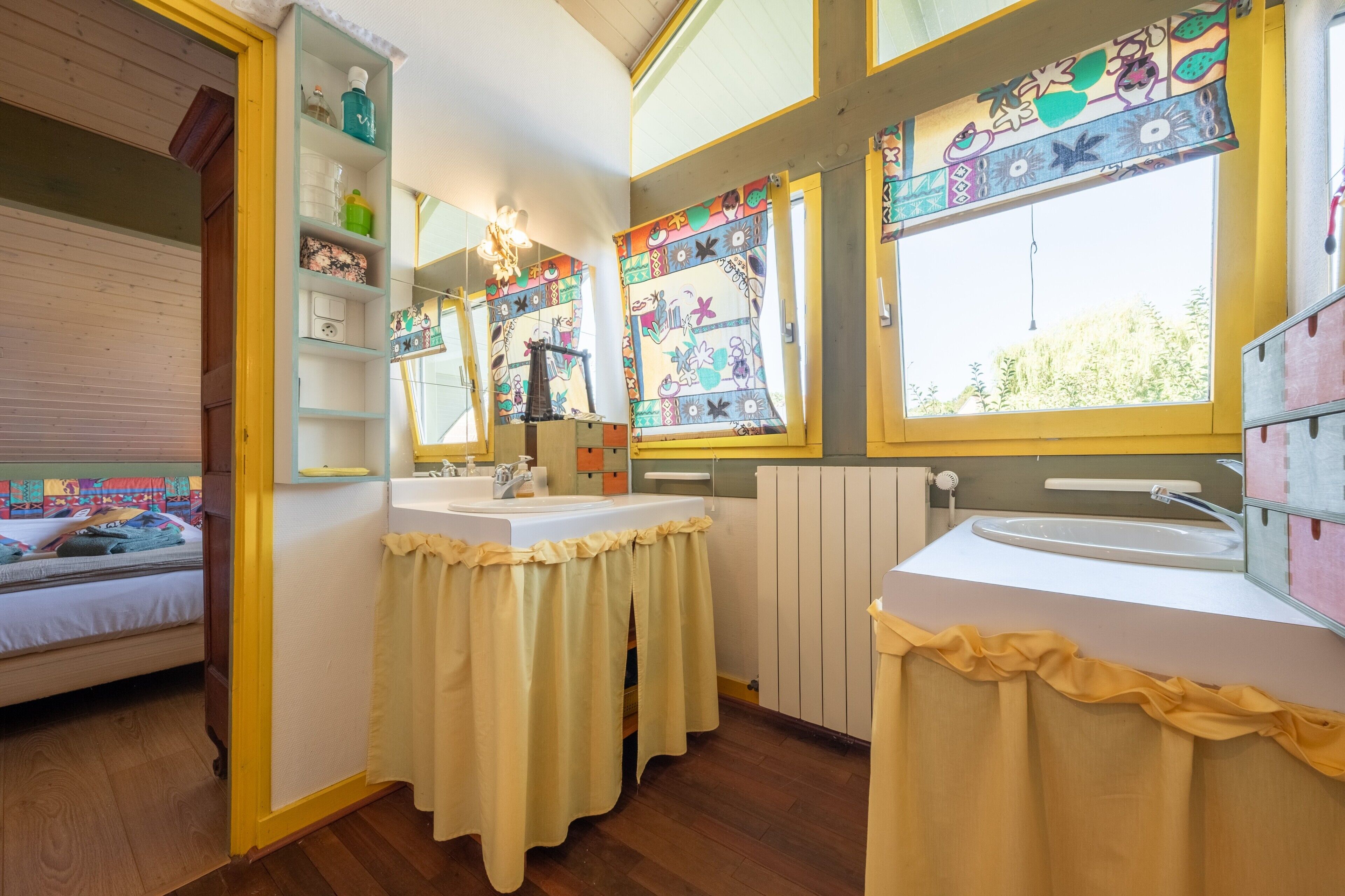 Een kamer met een bed, een raam met een kleurrijk gordijn, een wastafel en een spiegel.