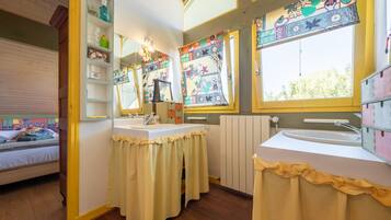 Een kamer met een bed, een raam met een kleurrijk gordijn, een wastafel en een spiegel.