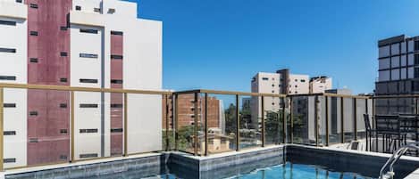 A rooftop pool with a glass barrier, surrounded by modern buildings with a mix of red and white facades.