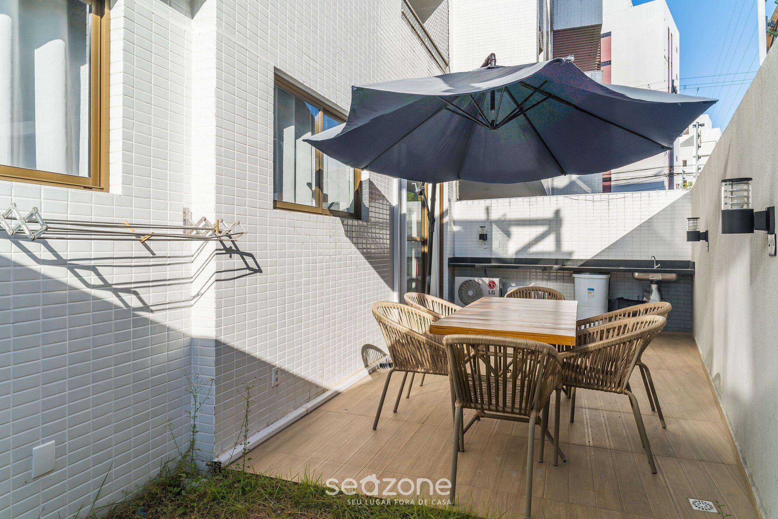 Une terrasse avec une table et des chaises, un grand parasol et un étendoir à linge.