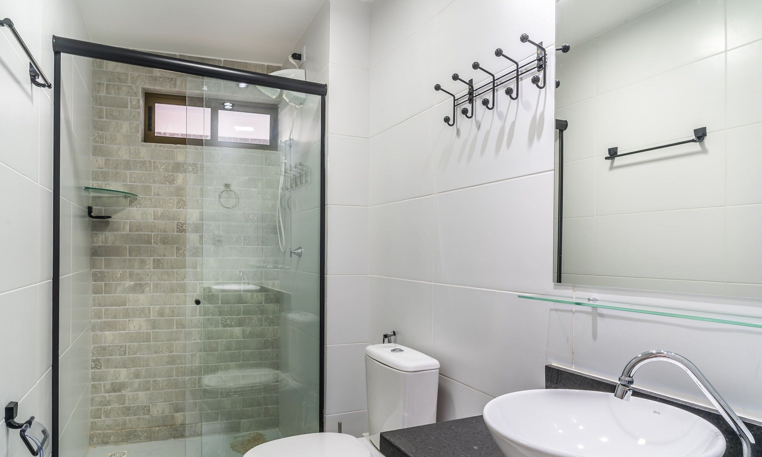 A modern bathroom with a glass-enclosed shower, a white sink, and a mirror with a towel rack.