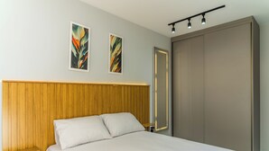 Un dormitorio moderno con cabecera de madera, cama con ropa blanca, dos cuadros abstractos en la pared y un armario con puerta corredera.
