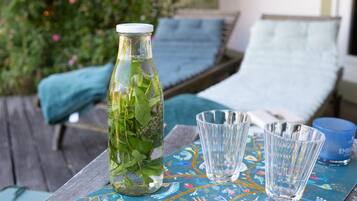 Una botella de vidrio con hojas de menta, dos vasos transparentes y una vela azul sobre una mesa de madera con mantel colorido.