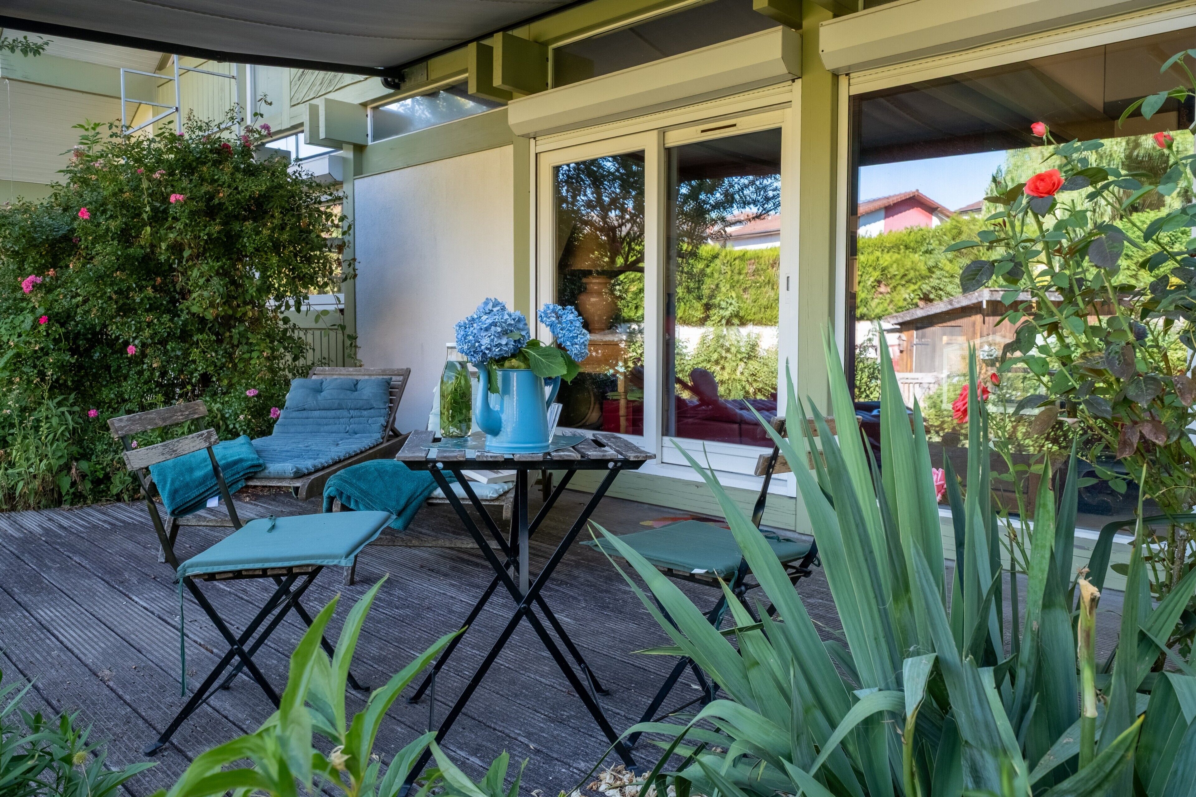 Une terrasse extérieure avec une table et des chaises, entourée de verdure et offrant une vue sur un quartier résidentiel.