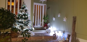 A decorated indoor space with a Christmas tree, a wooden bench, and a door with vertical blinds. - Room with Private Bathroom and Balcony by the Canal (Charmes)
