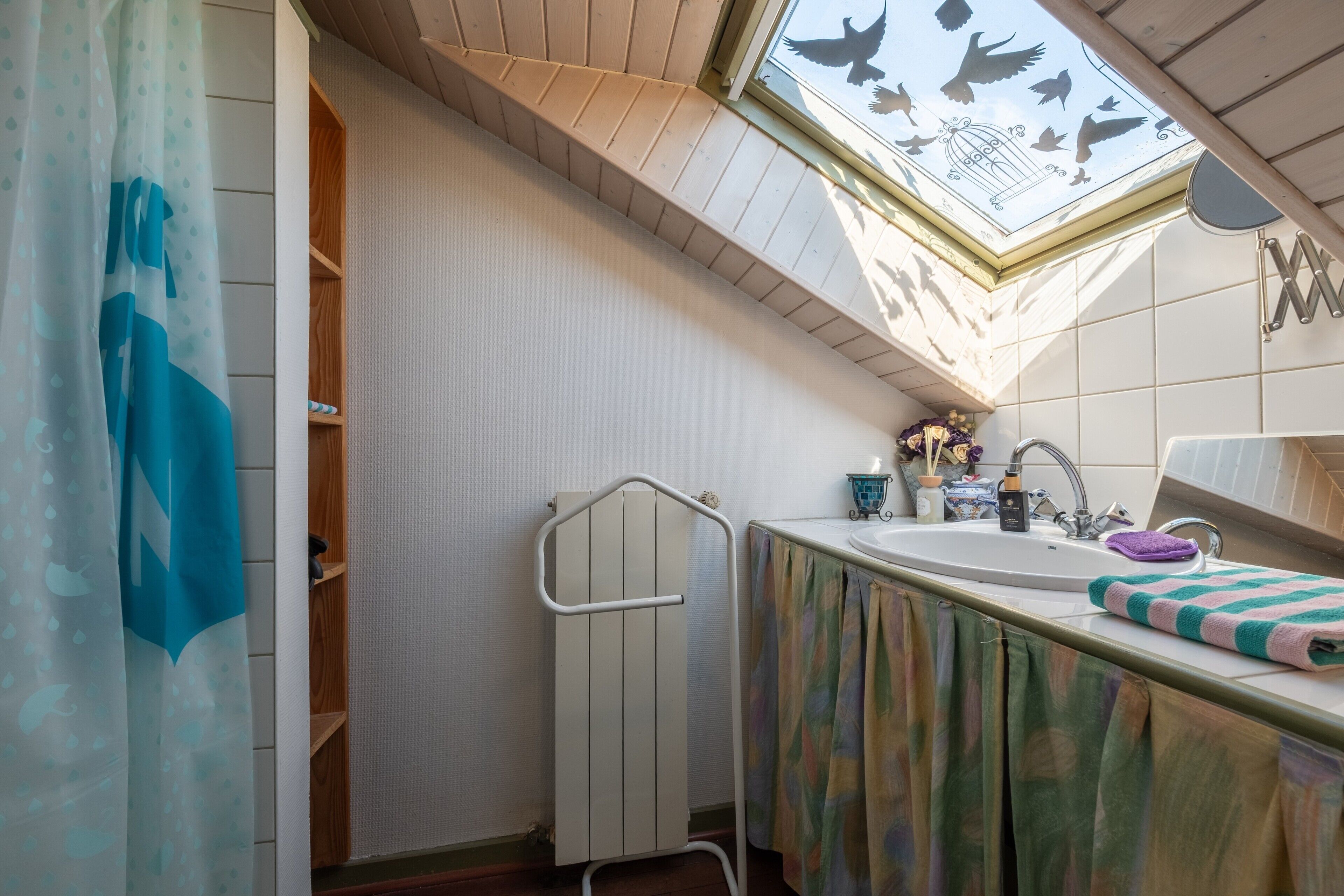Une salle de bain avec un puits de lumière, un rideau de douche, une serviette, un lavabo et une fenêtre.