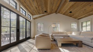 Un salón amplio con ventanas grandes, techo de madera y un sofá moderno.