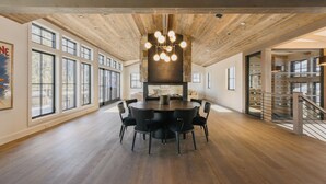 Un comedor amplio con una mesa redonda y sillas, ventanas grandes y techo de madera.