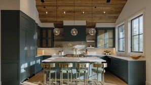 Una cocina moderna con una isla central, taburetes de bar y techo de madera.