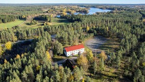 A large building surrounded by dense forest and a lake.