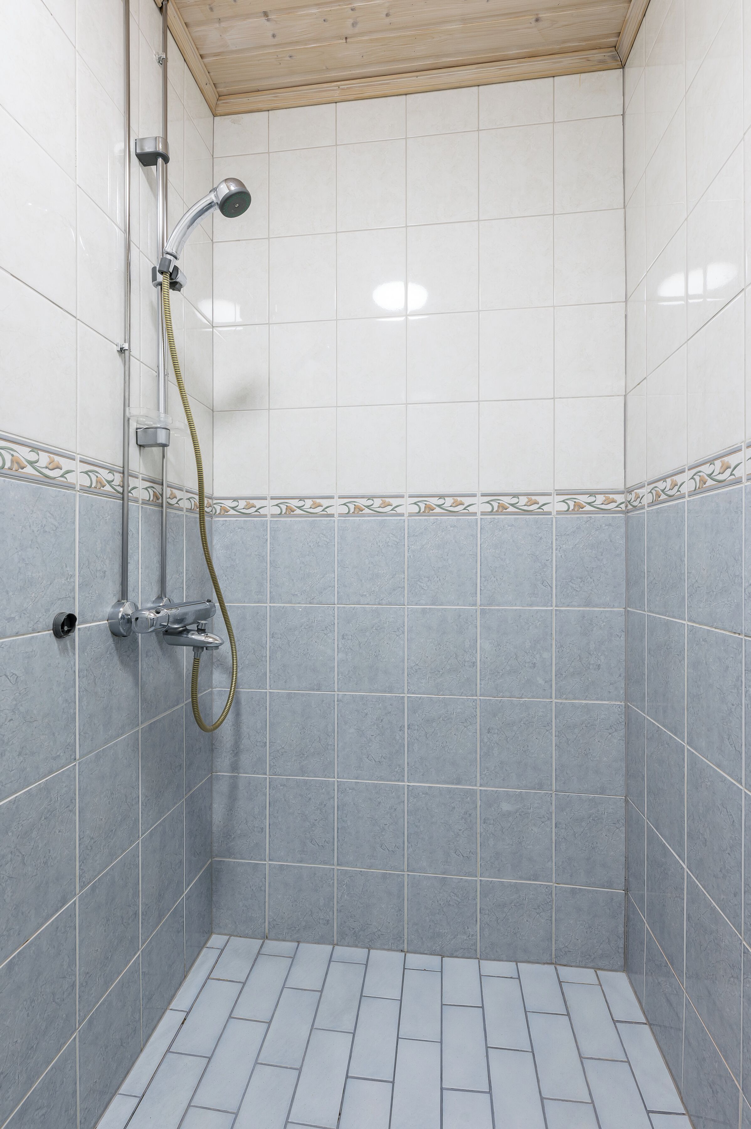 A small, tiled shower room with a showerhead and hose.