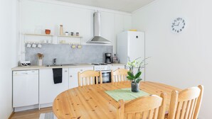 A modern kitchen with white cabinetry, a wooden dining table, and a clock on the wall.