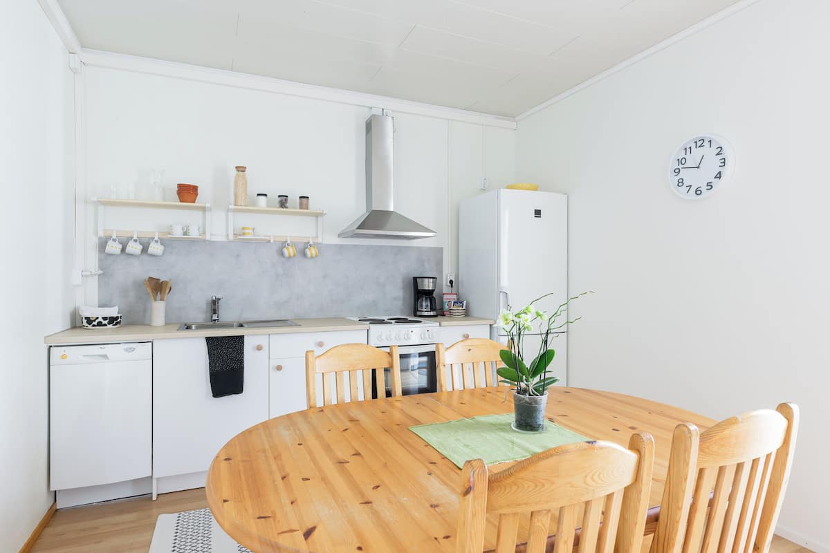 A modern kitchen with white cabinetry, a wooden dining table, and a clock on the wall.