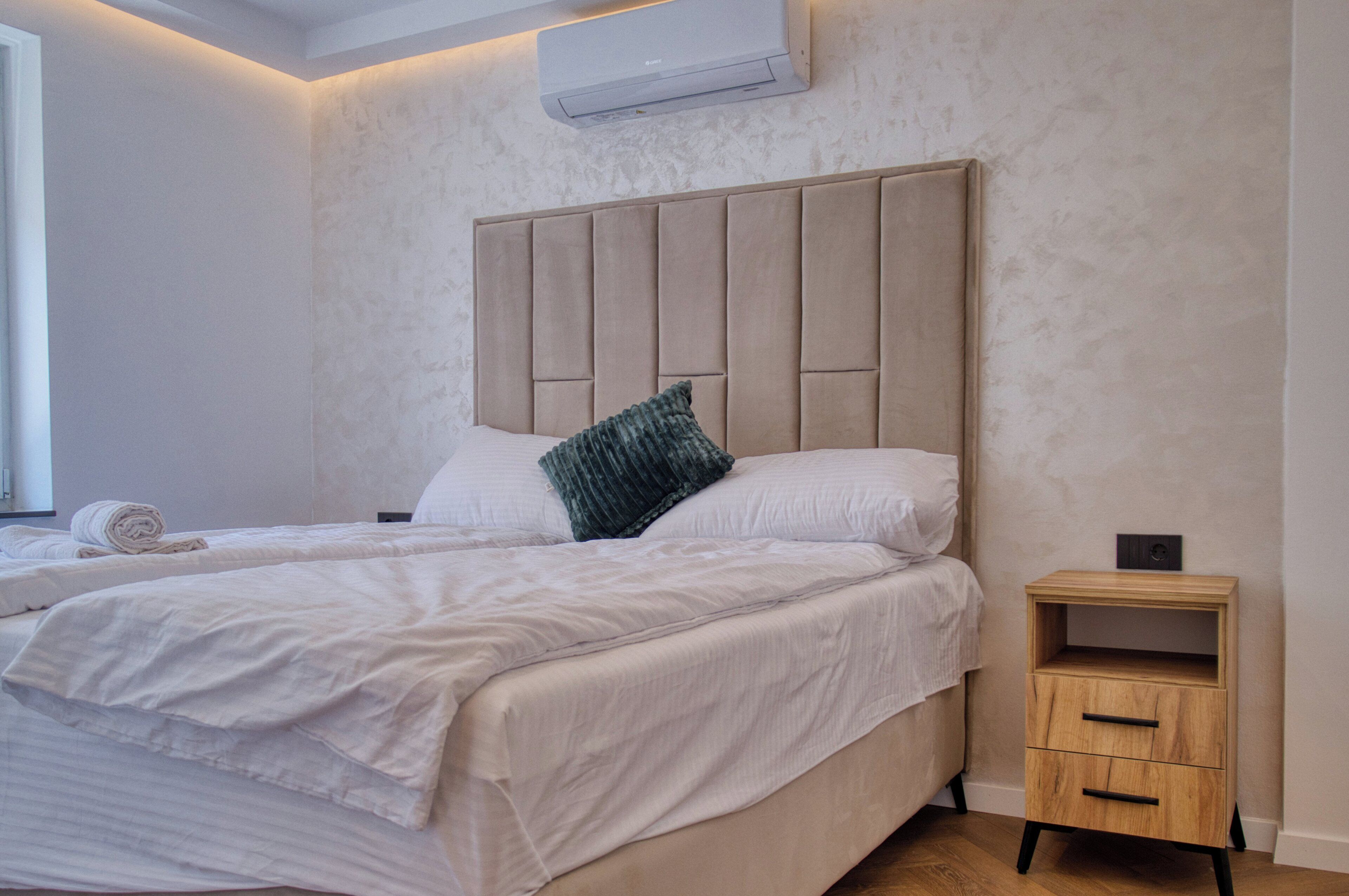 A double bed with a headboard, a bedside table with drawers, and a wall-mounted air conditioner.