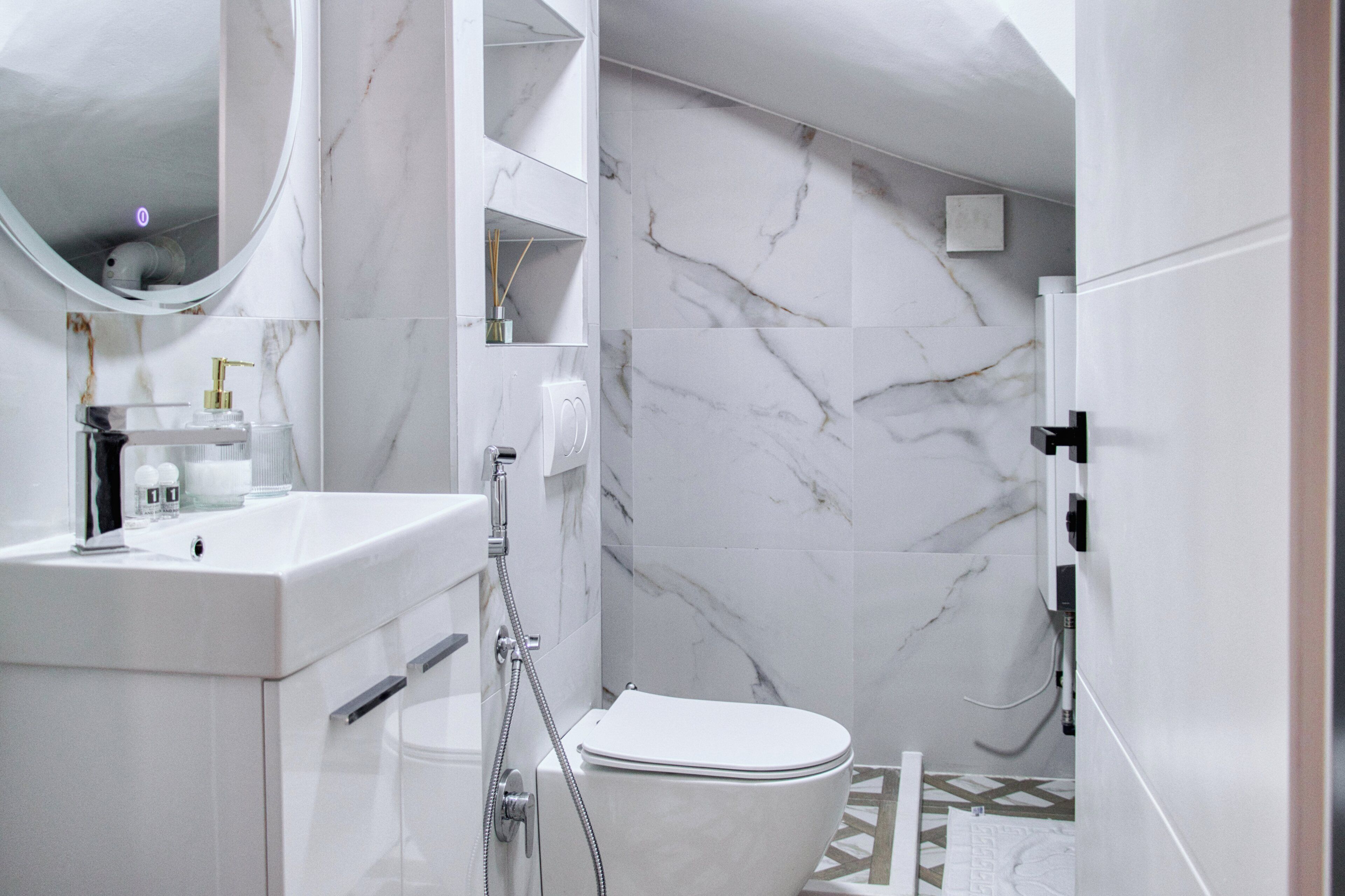 A modern bathroom with a white marble wall, a sink with a gold faucet, a toilet, and a shower area.
