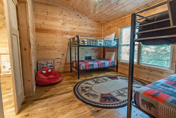 A wooden cabin room with bunk beds, a red bean bag chair, and a patterned rug.