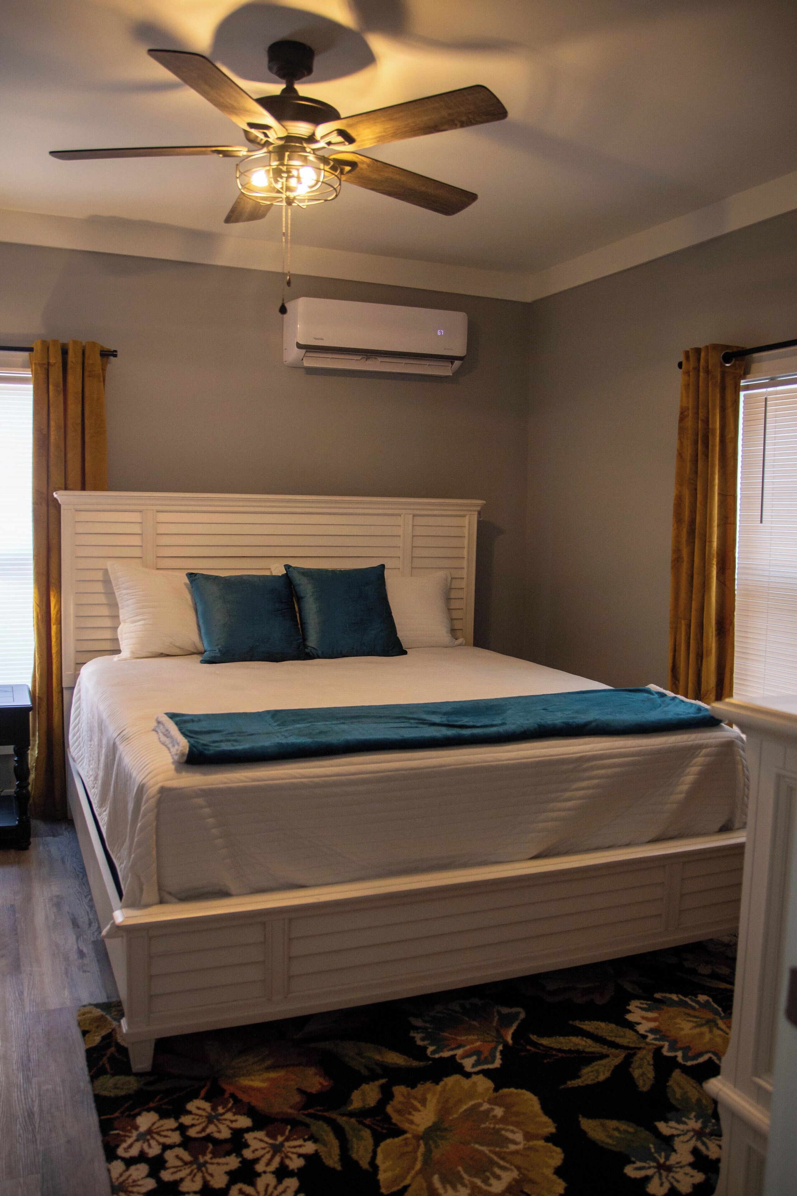 A neatly made bed with a white headboard, a ceiling fan, and an air conditioning unit on the wall.