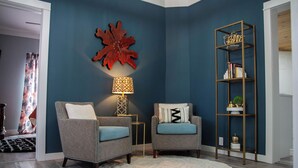 Un salon comprenant deux fauteuils, un tapis rond, un élément décoratif mural, une lampe sur pied et une bibliothèque.