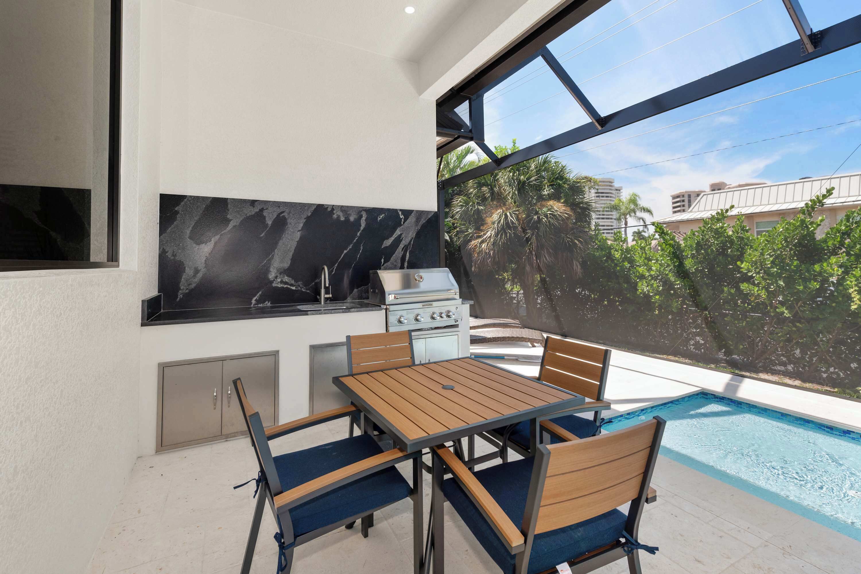 A modern kitchen with a marble backsplash, a built-in stove, and a dining area with a pool view.