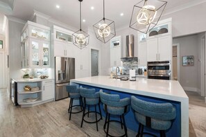 A modern kitchen with white cabinets, a large island with bar stools, stainless steel appliances, and geometric pendant lighting.
