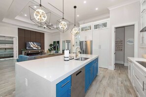 A modern kitchen with a large island, white cabinets, blue drawers, and a stainless steel refrigerator.