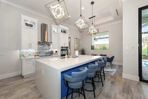 A modern kitchen with a central island, bar stools, and pendant lighting.