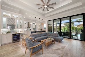 A modern living room with a sectional sofa, a coffee table, and a dining area with a kitchen in the background.