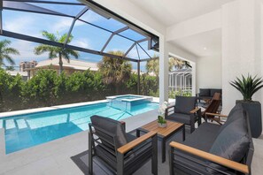 A modern outdoor pool area with a glass enclosure, seating, and a view of the surrounding greenery and buildings.