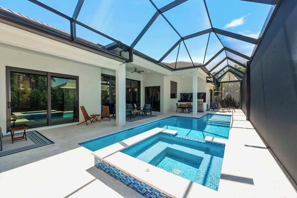 Un área de piscina exterior moderna con paredes de vidrio, un ventilador de techo y mobiliario de exterior.