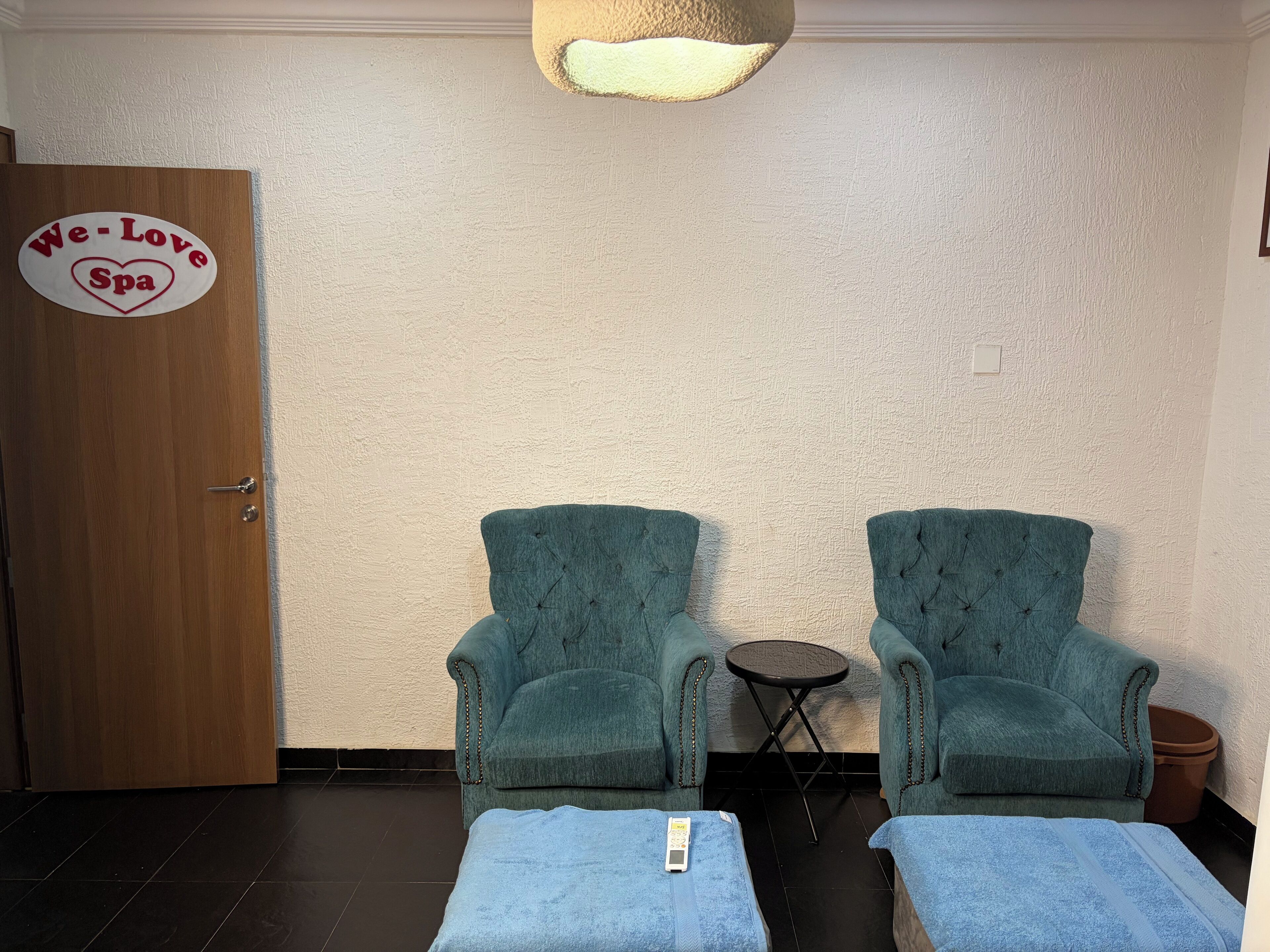 Un cuarto de spa con dos sillones y una mesita, un cartel en la pared y una puerta.