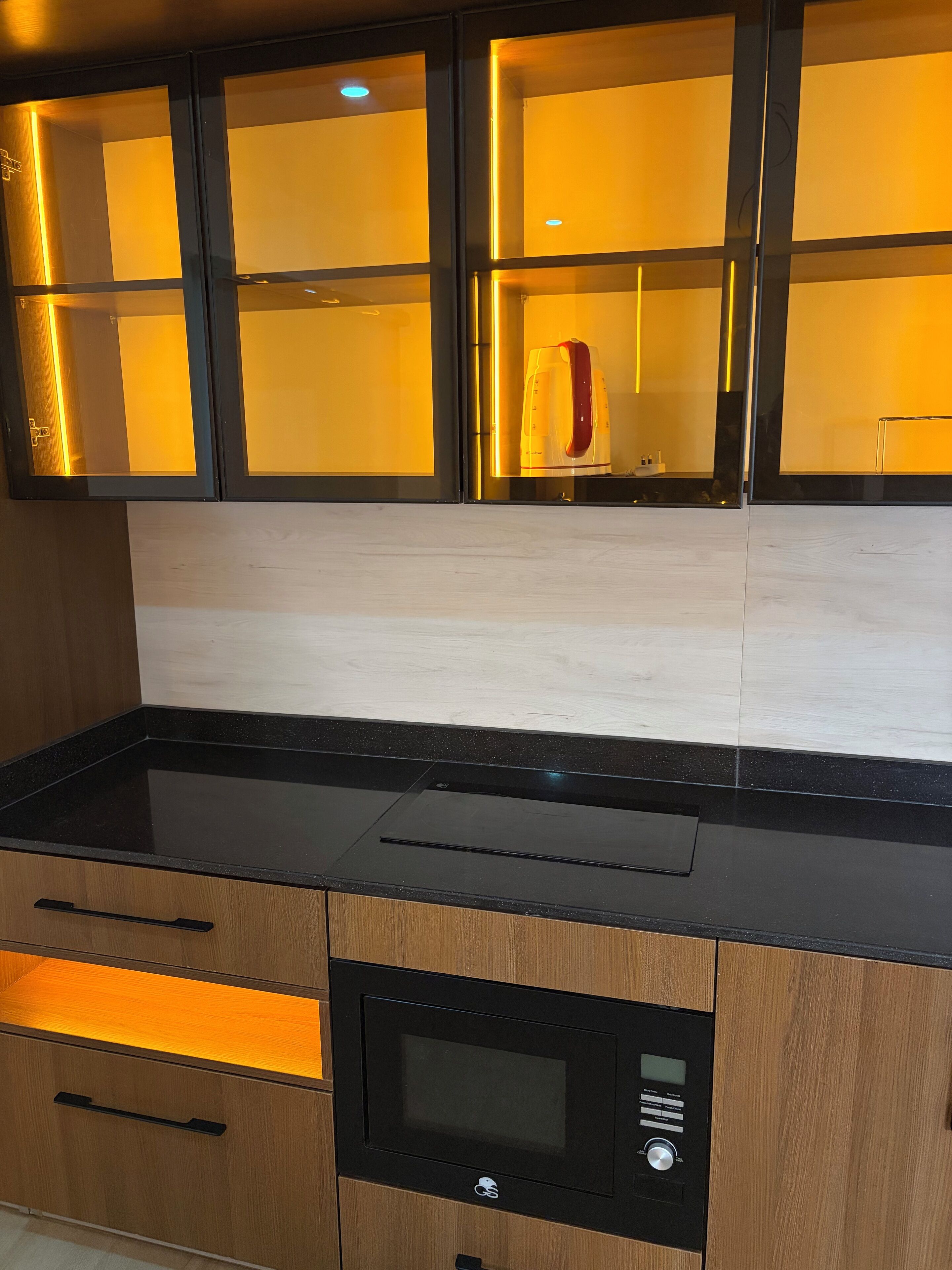 A modern kitchen with a black countertop, wooden cabinets, and a built-in microwave.