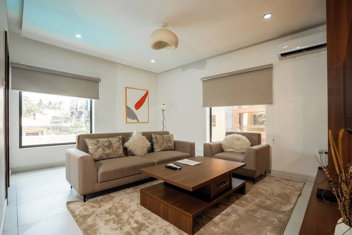 Una sala moderna con un conjunto de sofás, una mesa de centro y un ventanal con persianas.