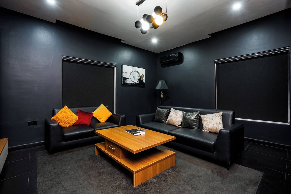 Una sala de estar moderna con dos sofás de cuero negro, una mesa de centro de madera y una alfombra gris.