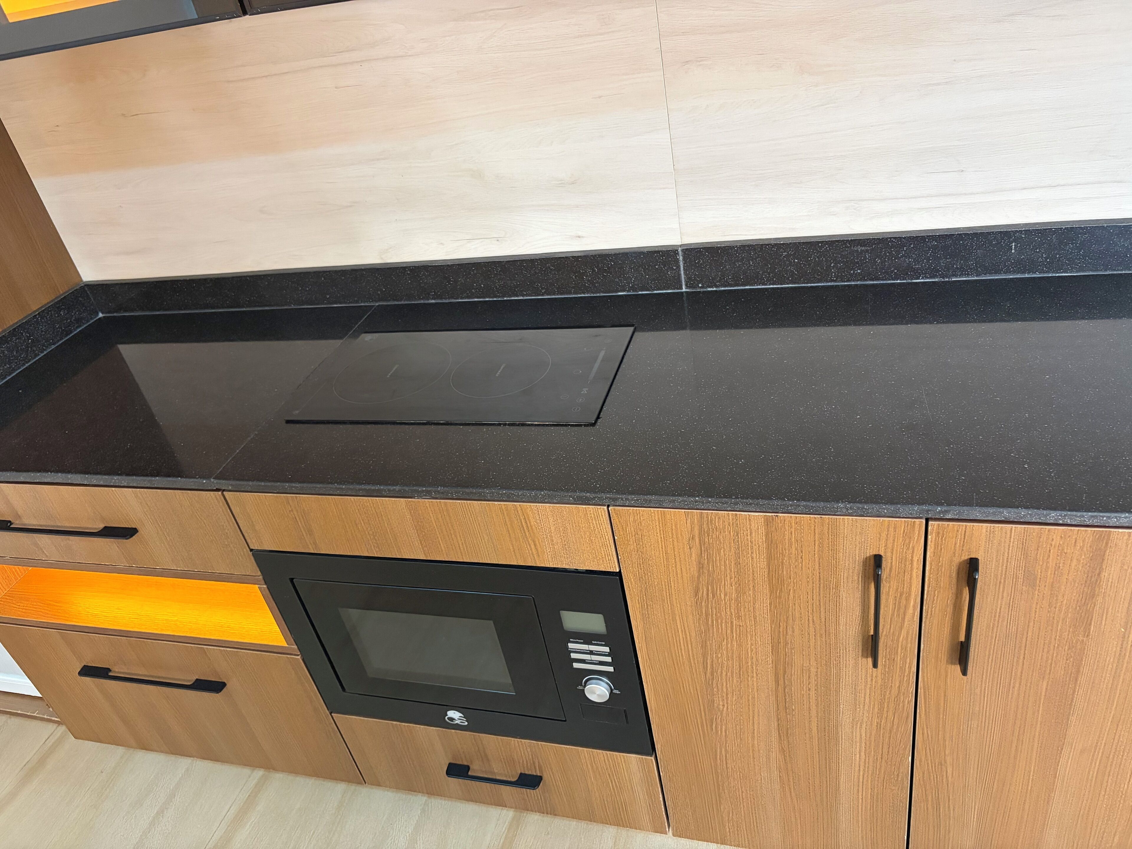 Una cocina con encimera negra, armarios de madera y horno empotrado.