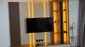 A modern entertainment unit with a flat-screen TV, wooden shelves, and integrated lighting. - COLOGNE RESIDENCE  (Abuja)