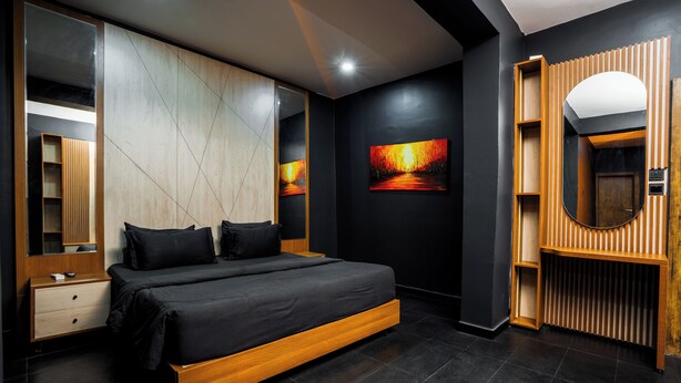 A modern bedroom with a large bed, a wooden nightstand, a built-in wardrobe, a large mirror, and a painting on the wall. - COLOGNE RESIDENCE  (Abuja)