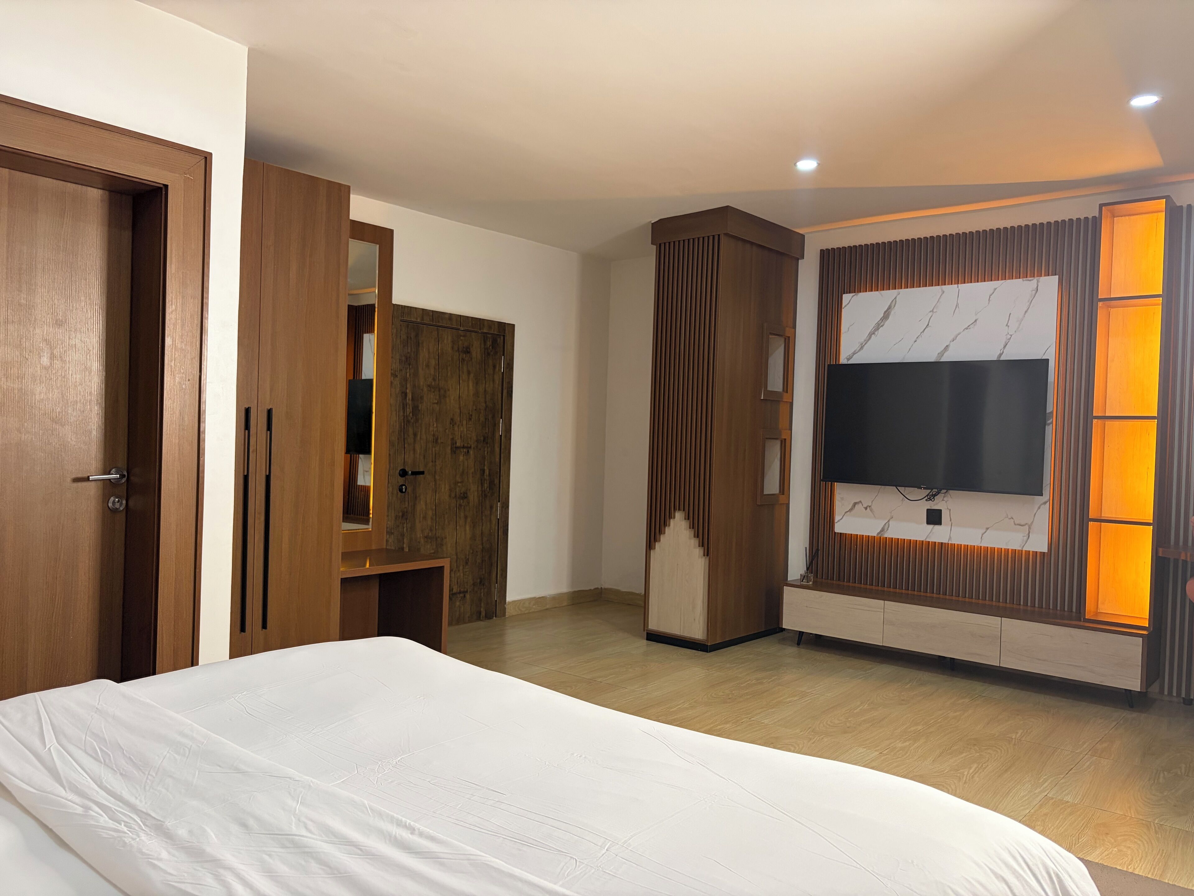 A bedroom with a large bed, wooden wardrobe, built-in TV, and a wall-mounted shelf.