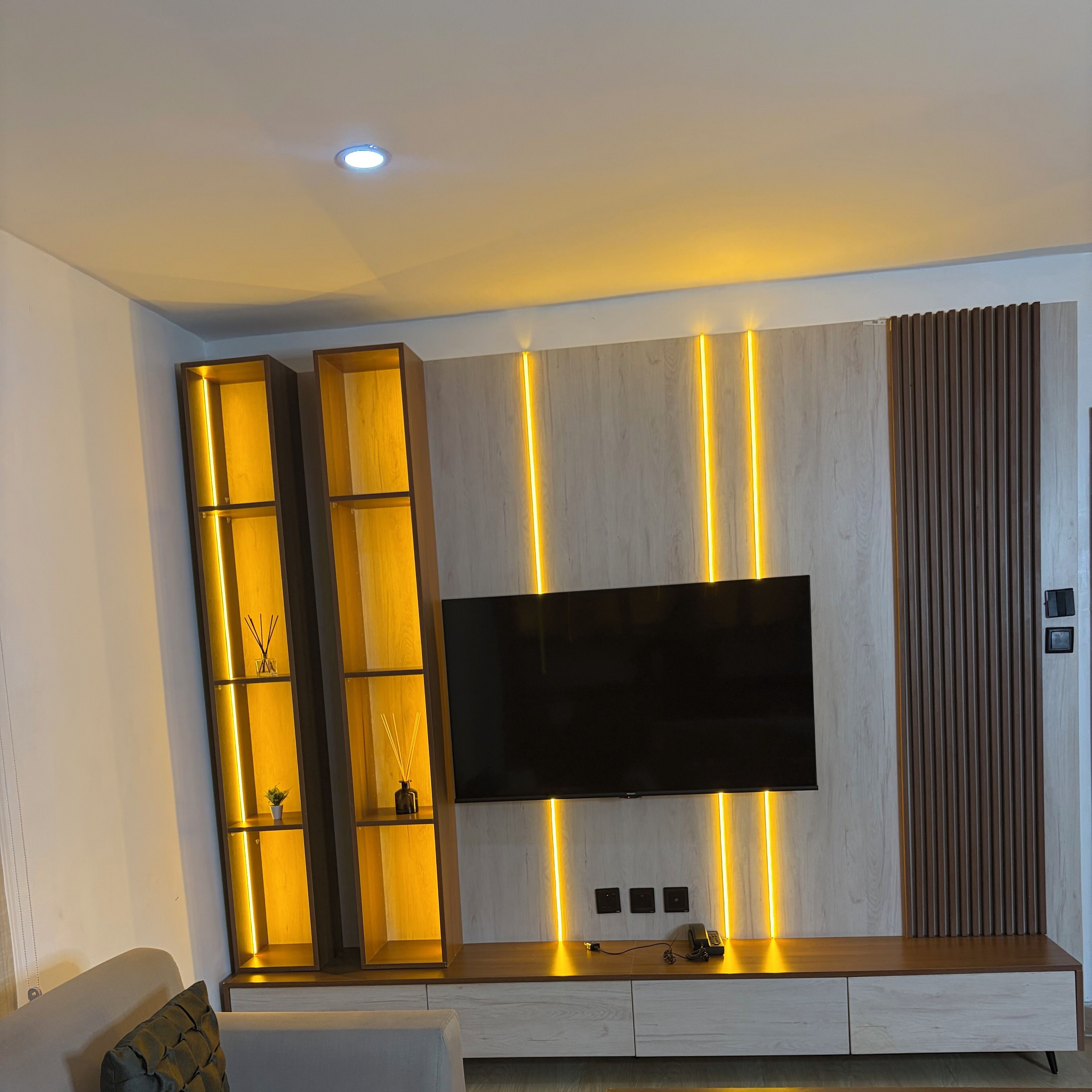 Una sala de estar moderna con un televisor de pantalla plana montado en una pared de madera, iluminada por luces LED verticales.