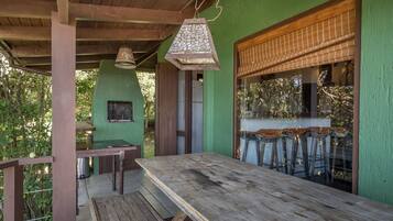 Um alpendre externo coberto com mesa de madeira e bancos, um lampião pendurado e uma parede verde.