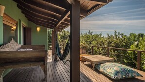 Une terrasse en bois avec un hamac, un banc en bois et une table agrémentée d’un coussin à motifs floraux.