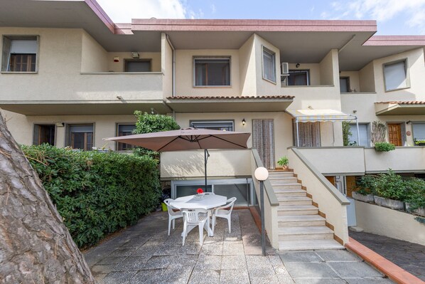A residential building with a patio area featuring a table and chairs, a covered outdoor seating area, and a staircase.
