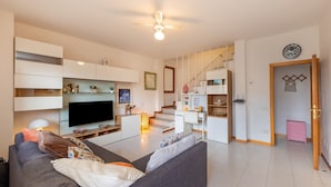Ein modernes Wohnzimmer mit Flachbildfernseher, grauem Sofa und einer Treppe zu einem Küchenbereich.