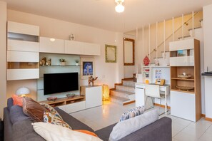 A modern living room with a flat-screen TV, a sofa, a coffee table, a staircase, and built-in shelving.