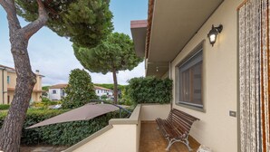 Ein Balkon mit einer Bank, einem Baum und einer Wandleuchte.