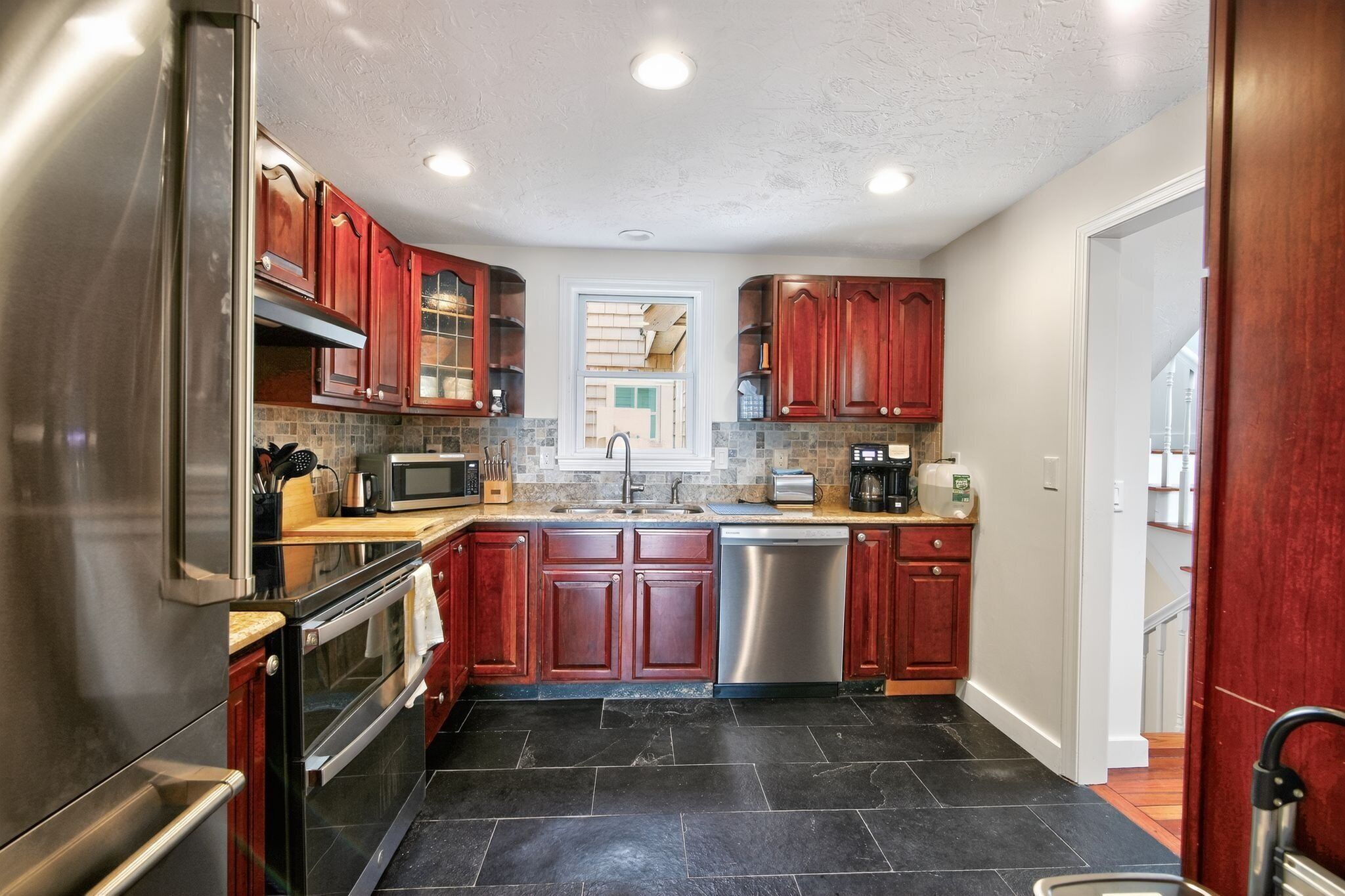A modern kitchen with stainless steel appliances, dark stone flooring, and wooden cabinetry.
