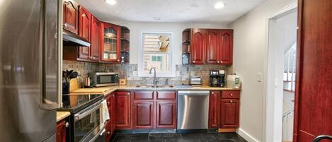 A modern kitchen with stainless steel appliances, dark stone flooring, and wooden cabinetry.