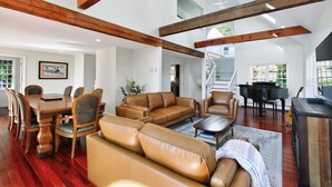 A spacious living area with a dining table, leather sofas, a piano, and a staircase leading to an upper level. - Ocean Views & Private Beach 3br Nature Escape 3 Bedroom Villa (Plymouth)
