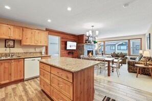 A modern kitchen with wooden cabinets, granite countertops, and a built-in island. There is a dining area with a table and chairs, and a living room with a sofa and a fireplace. - 2 Bedroom Kirkwood Condo Across the Street from Village 2 Condo (Kirkwood)
